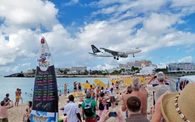 Crowd watches airplane land just above the beach at Maho Beach, St. Maarten, with clear skies and turquoise water. One of the must do things to do in St Martin / St Maarten