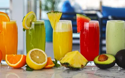 Colorful tropical fruit juices in tall glasses garnished with fresh fruit slices on a countertop.