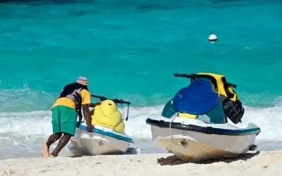 Man pushing jet skis into turquoise water on a sandy beach in St Maarten.