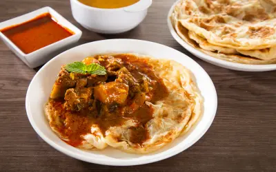Caribbean roti plate with curry stew and folded flatbread on a wooden table. Things to do in St Martin