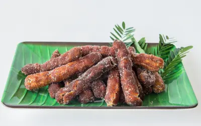 Sugar-coated tamarind sticks served on a green leaf-lined platter.