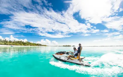 Teen riders speeding across calm turquoise waters on a jet ski near a tropical shoreline, one of the fun things to do in St Martin / St Maarten