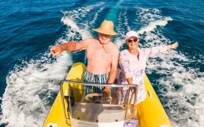 Smiling couple riding a small yellow speedboat on clear blue water with a trail of waves behind them. Water activities can be great things to do in St Martin / St Maarten whatever your age