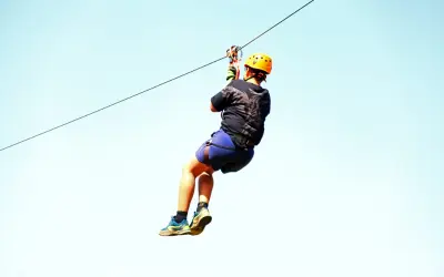 Person ziplining high in the air under a bright blue sky at Rockland Estate, St Maarten. Adventurous things to do in St Martin / St Maarten