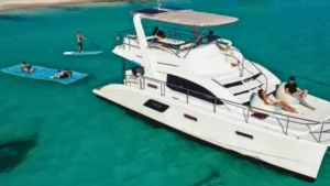 Private catamaran anchored in clear Caribbean water with guests paddleboarding and relaxing on a floating mat