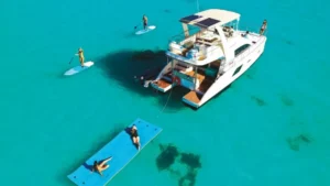 Aerial view of a private catamaran charter with paddleboarders and guests relaxing on a floating mat in turquoise water