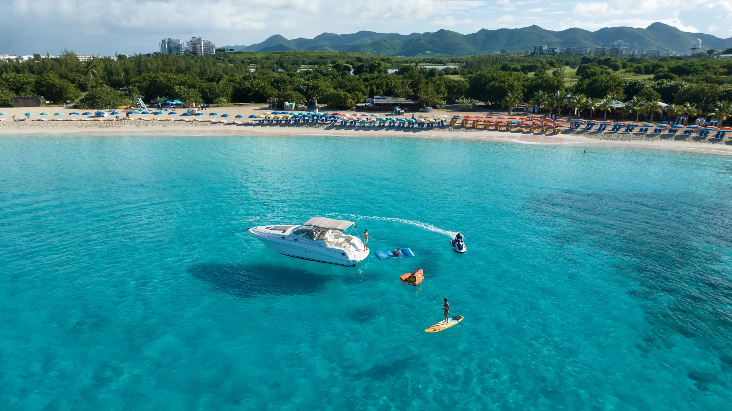 Aerial shot of yacht anchored close to a beautiful beach with guests enjoying water activities