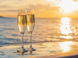 Two champagne glasses standing on a ledge with the sea and sunset in the background