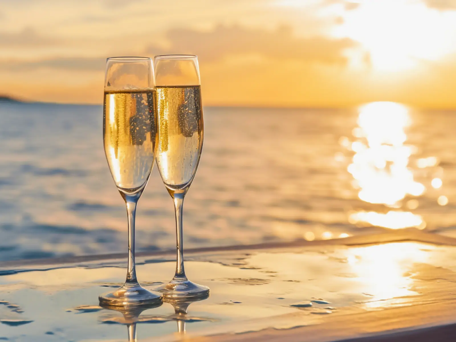 Two champagne glasses standing on a ledge with the sea and sunset in the background