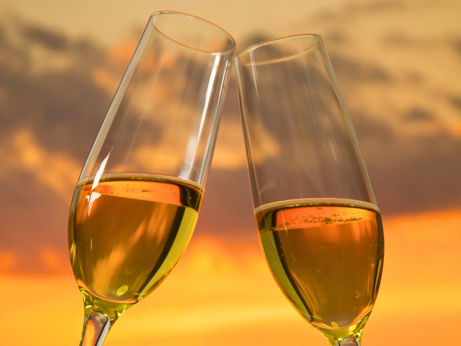 Two champagne flutes clinking together against a golden sunset sky