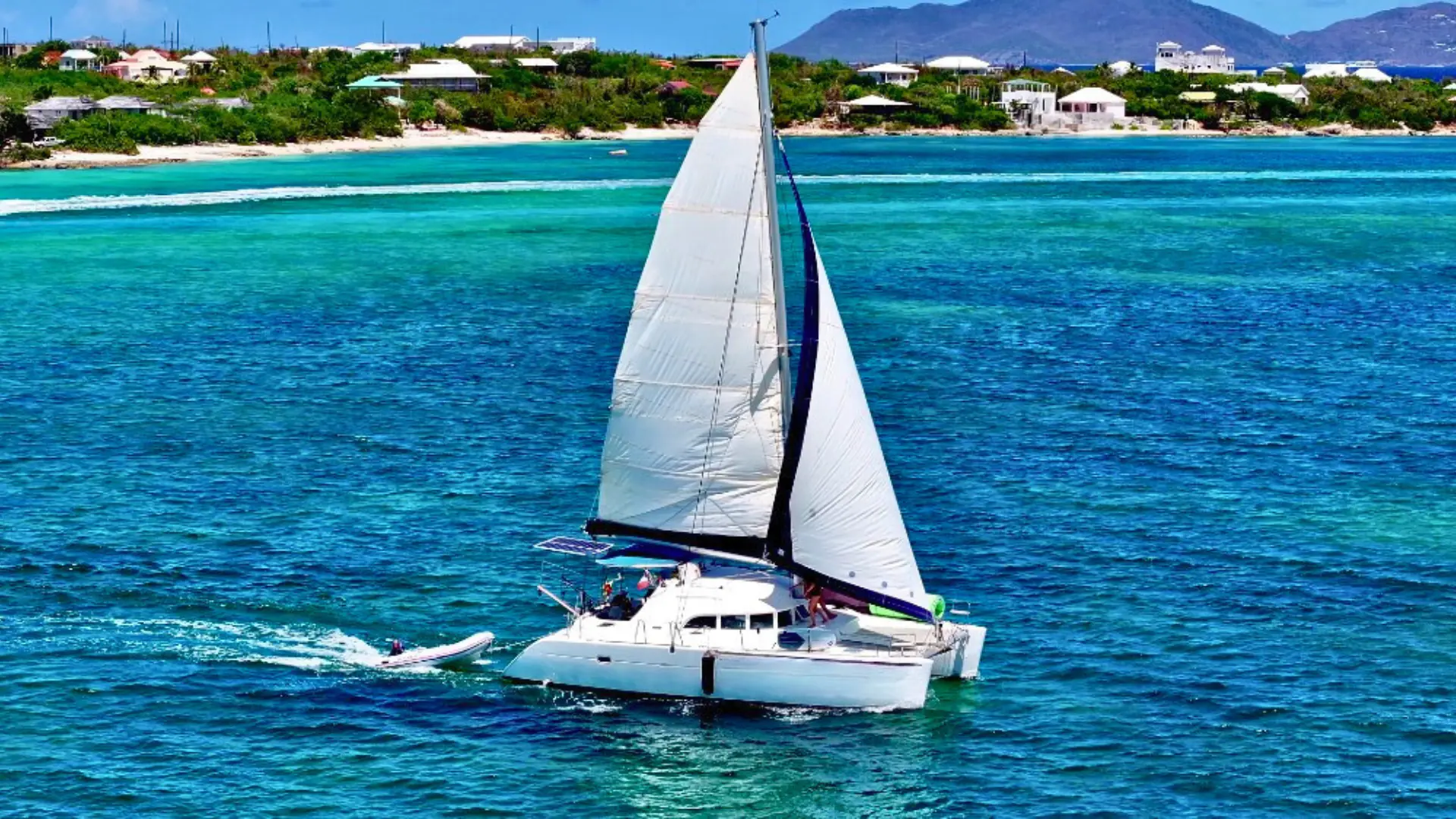 Catamaran sailing along St Martin’s coastline with tender boat behind