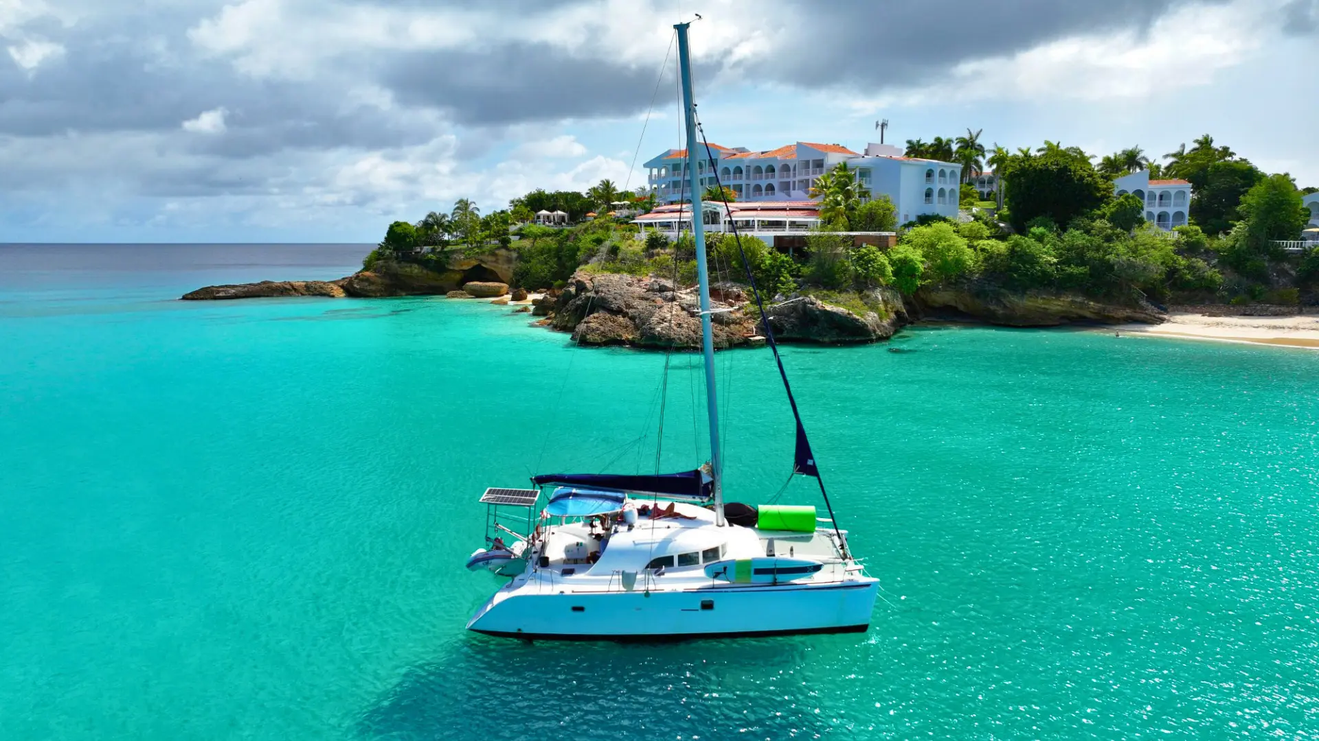 Catamaran cruising in crystal-clear turquoise water near luxury villas in St Martin
