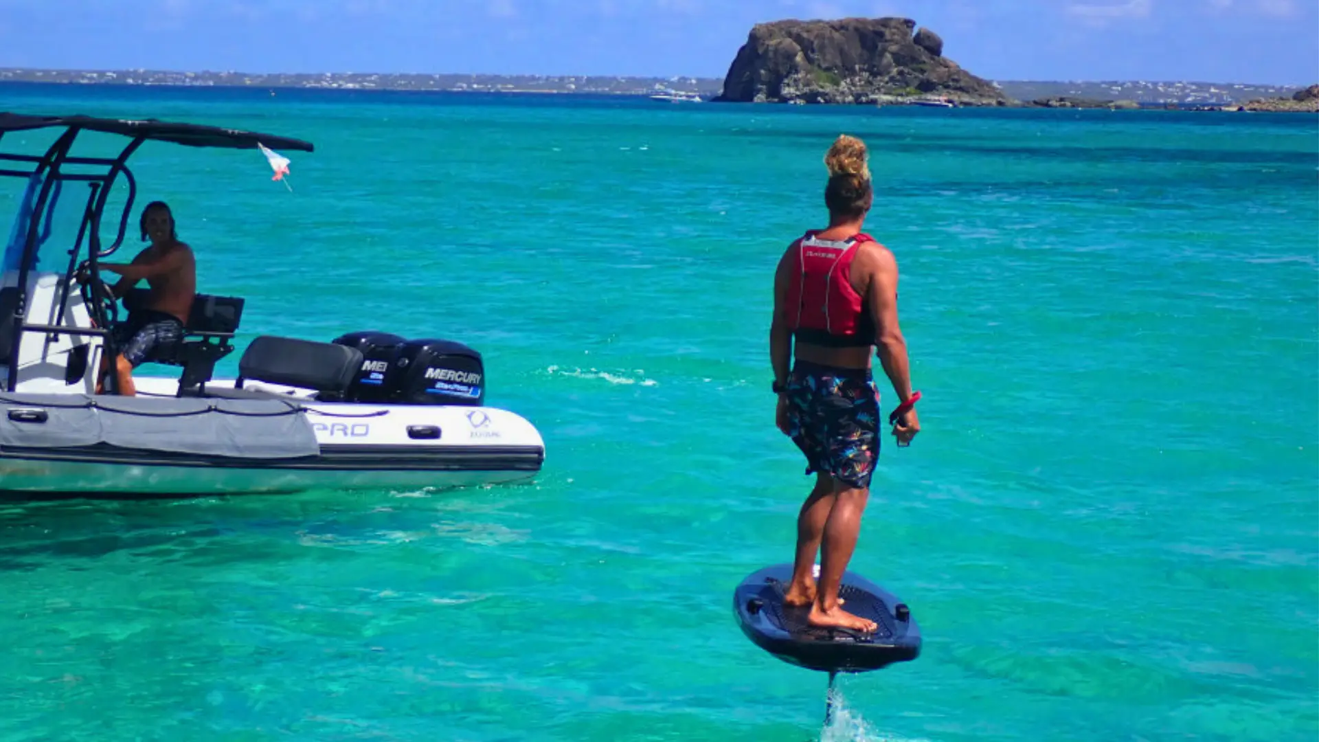 E-foil rider hovering above turquoise water with support boat nearby in St Martin