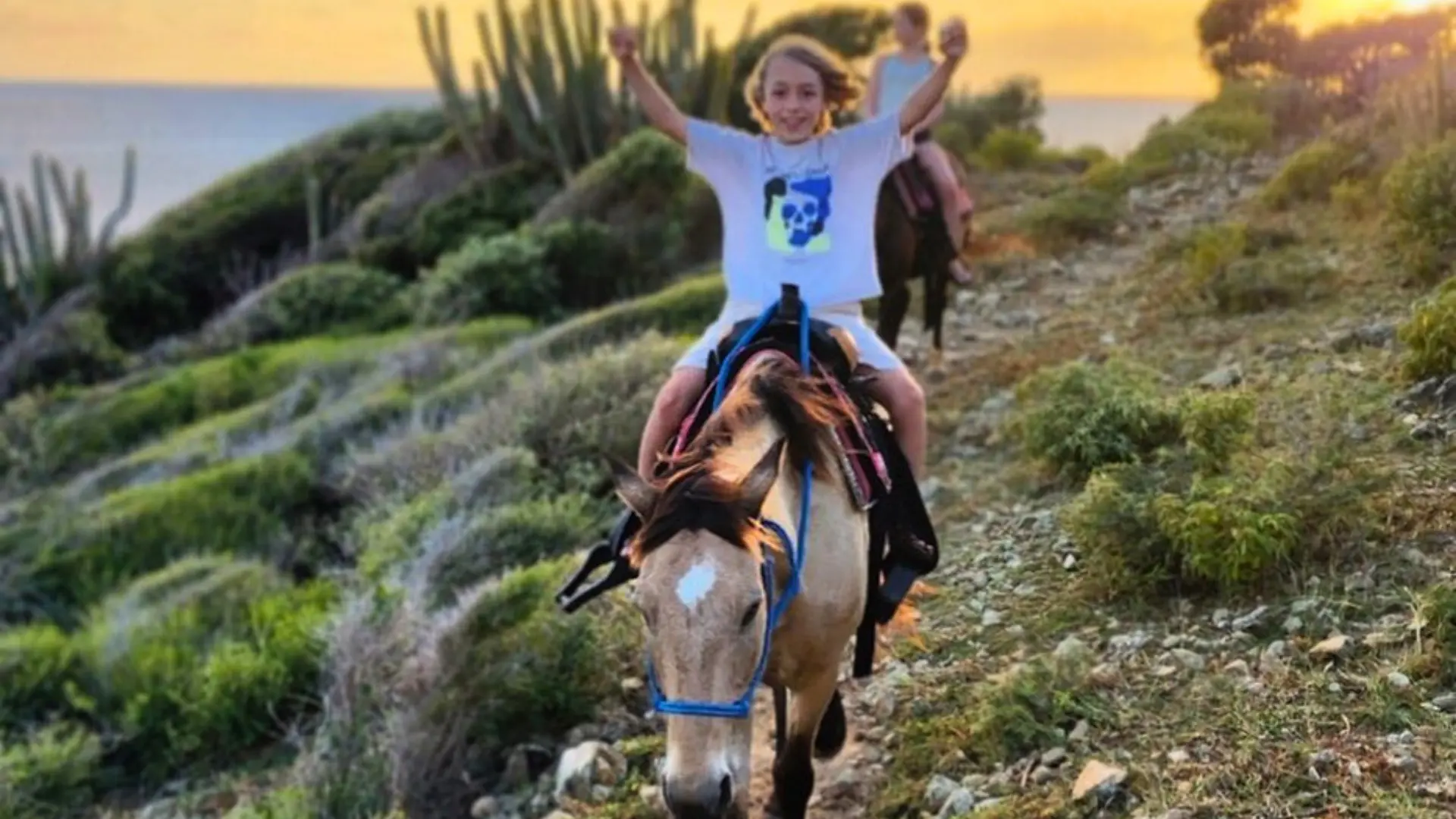 Child riding a horse along a coastal trail at sunset in St Maarten
