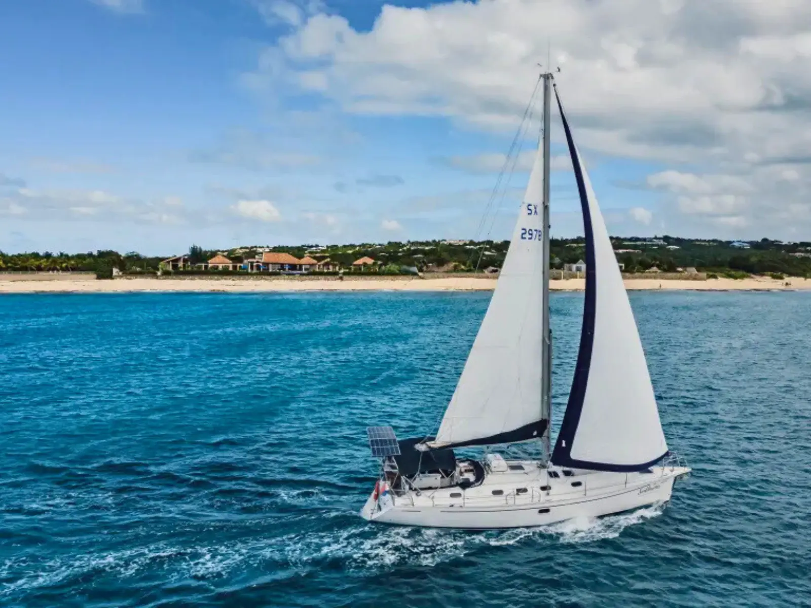 Private monohull sailing yacht cruising in turquoise waters along the St Maarten coastline on a sunny day