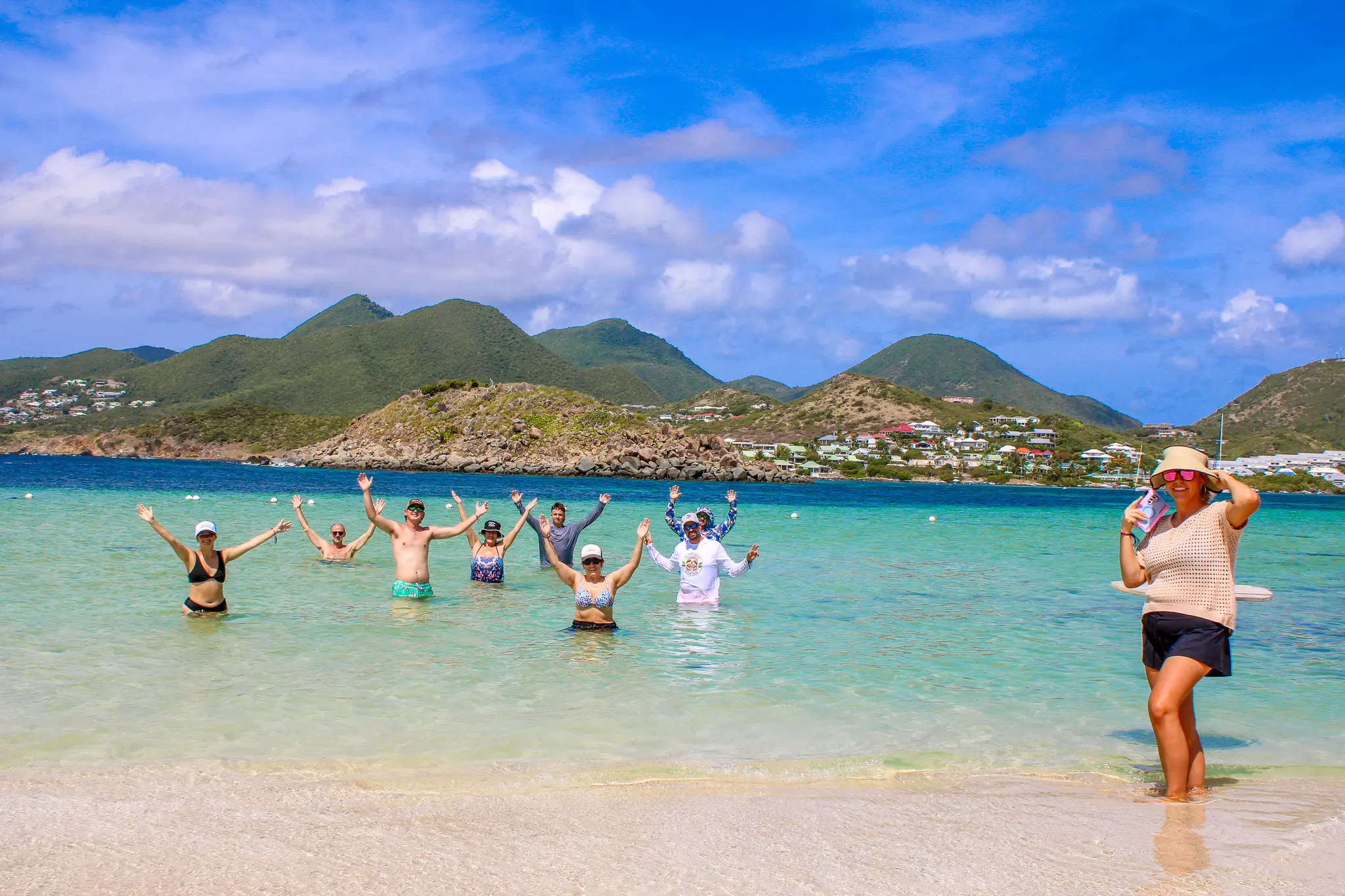 Guests standing in the shallow turquoise water at Pinel Island with scenic hills in the background