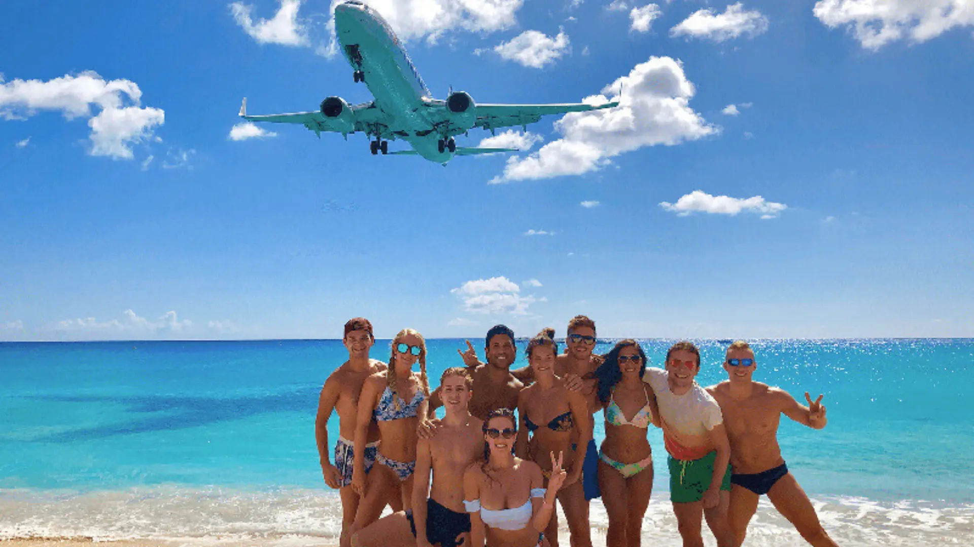 Group of friends posing on Maho Beach with airplane flying overhead in St Maarte