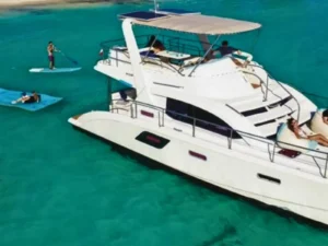 Catamaran stern view with guests lounging and paddleboarding in clear Caribbean sea