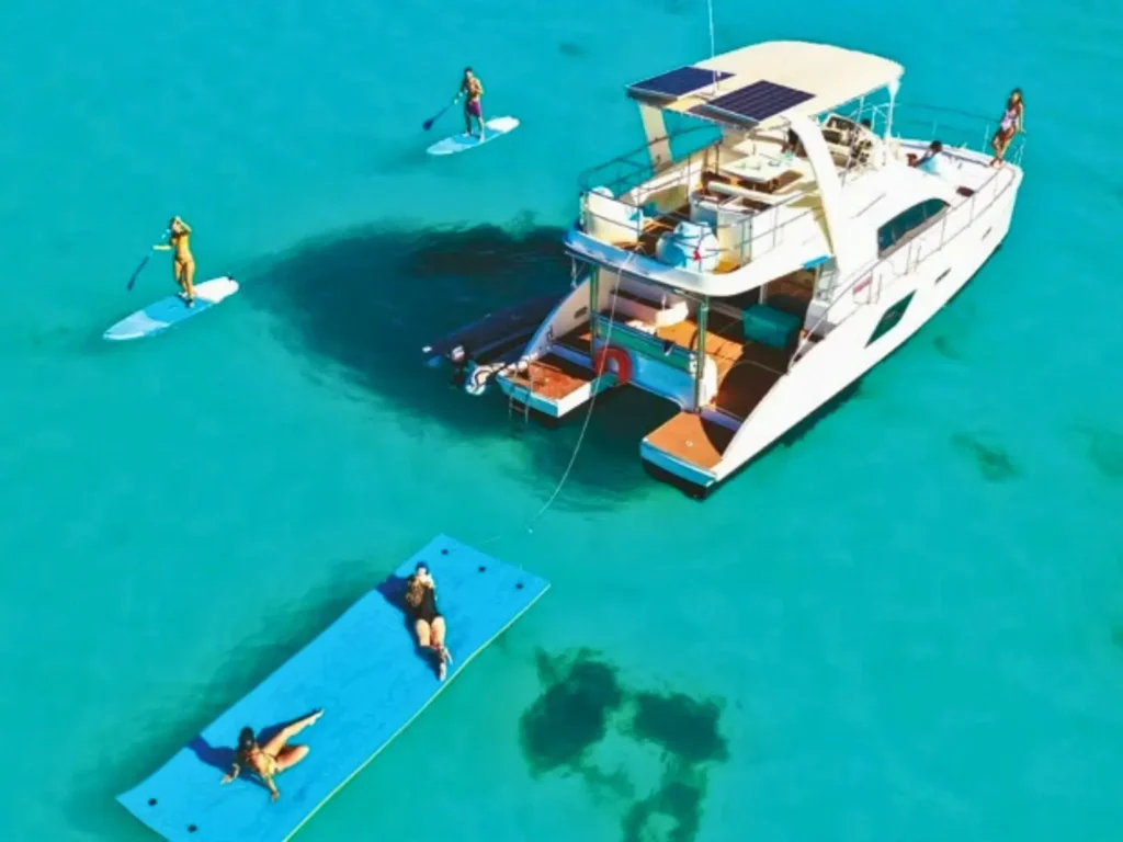 Catamaran anchored in shallow turquoise water with paddleboards and floating mat