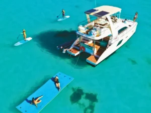 Catamaran anchored in shallow turquoise water with paddleboards and floating mat