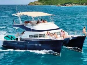 Power catamaran cruising near the coastline with guests seated along the bow