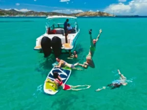 Guests swimming and paddleboarding behind private boat in St Martin