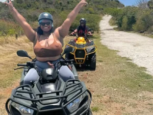Happy rider raising arms while riding an ATV on a scenic trail in St Maarten with another quad following