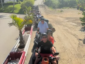 Group of riders on ATVs traveling along mixed paved and dirt roads during a St Maarten island tour