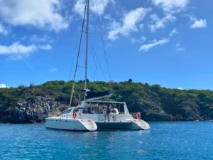 Private sailing catamaran anchored off the coast of St Maarten with rocky shoreline in the background