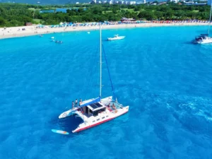 Drone view of a private catamaran anchored off a busy St Maarten beach with umbrellas, swimmers, and boats nearby