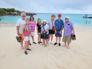 Group of travelers standing together on a white-sand beach with calm turquoise water in St Martin