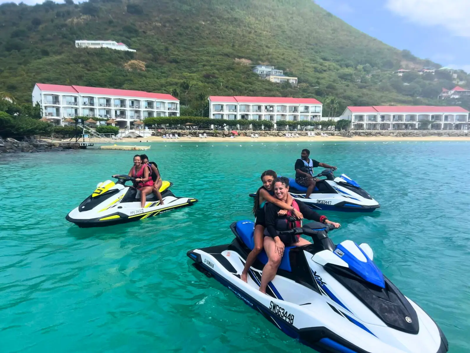 Jet ski riders posing on the water near St Martin resorts with shallow turquoise sea and beachfront hotels