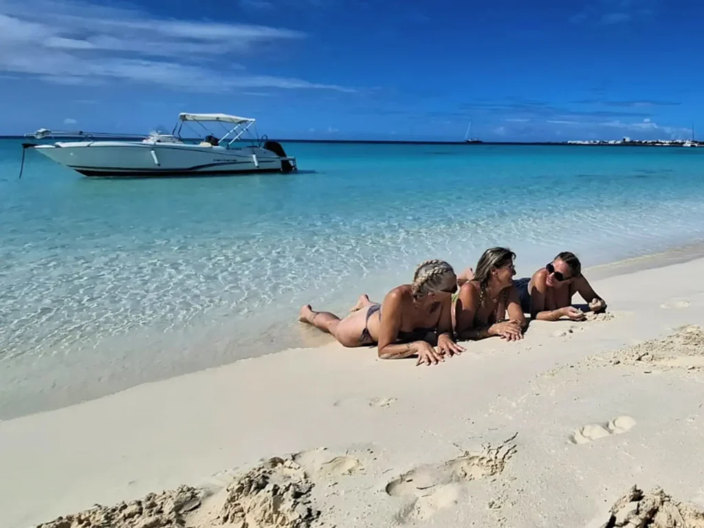 Guests relaxing on a white sand beach with private boat anchored in turquoise water in Anguilla