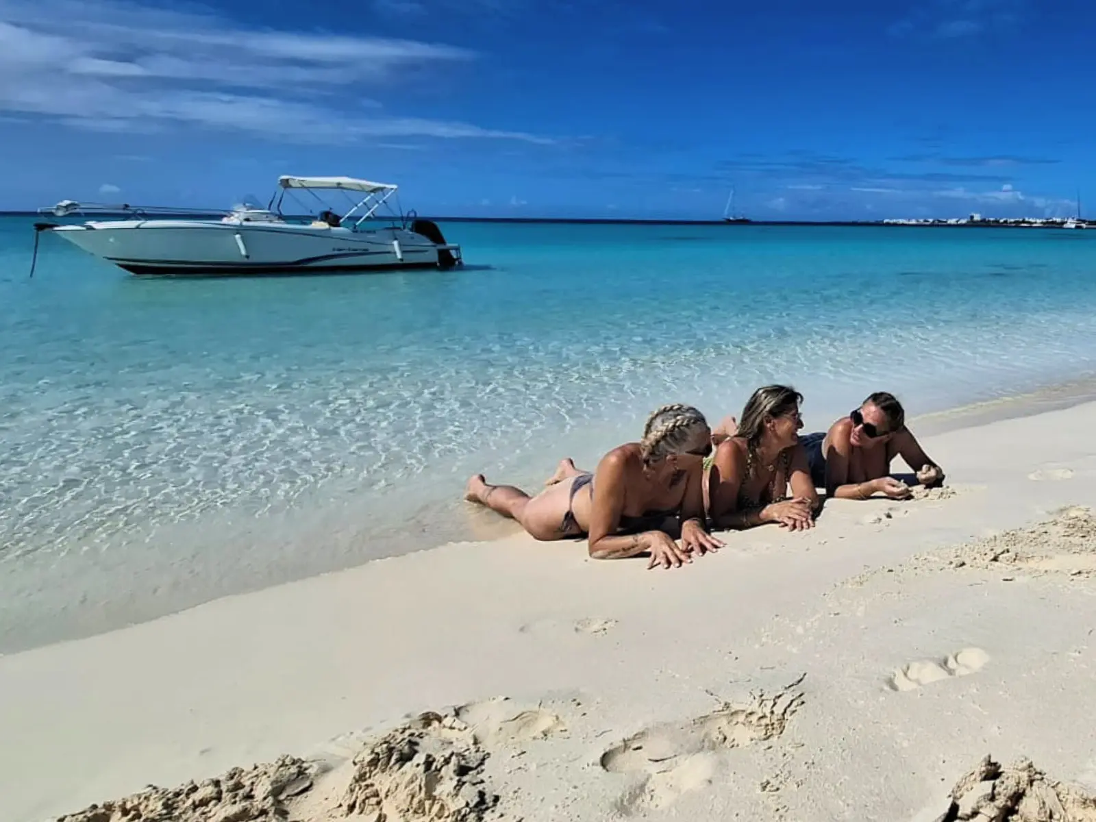 Guests relaxing on a white sand beach with private boat anchored in turquoise water in Anguilla