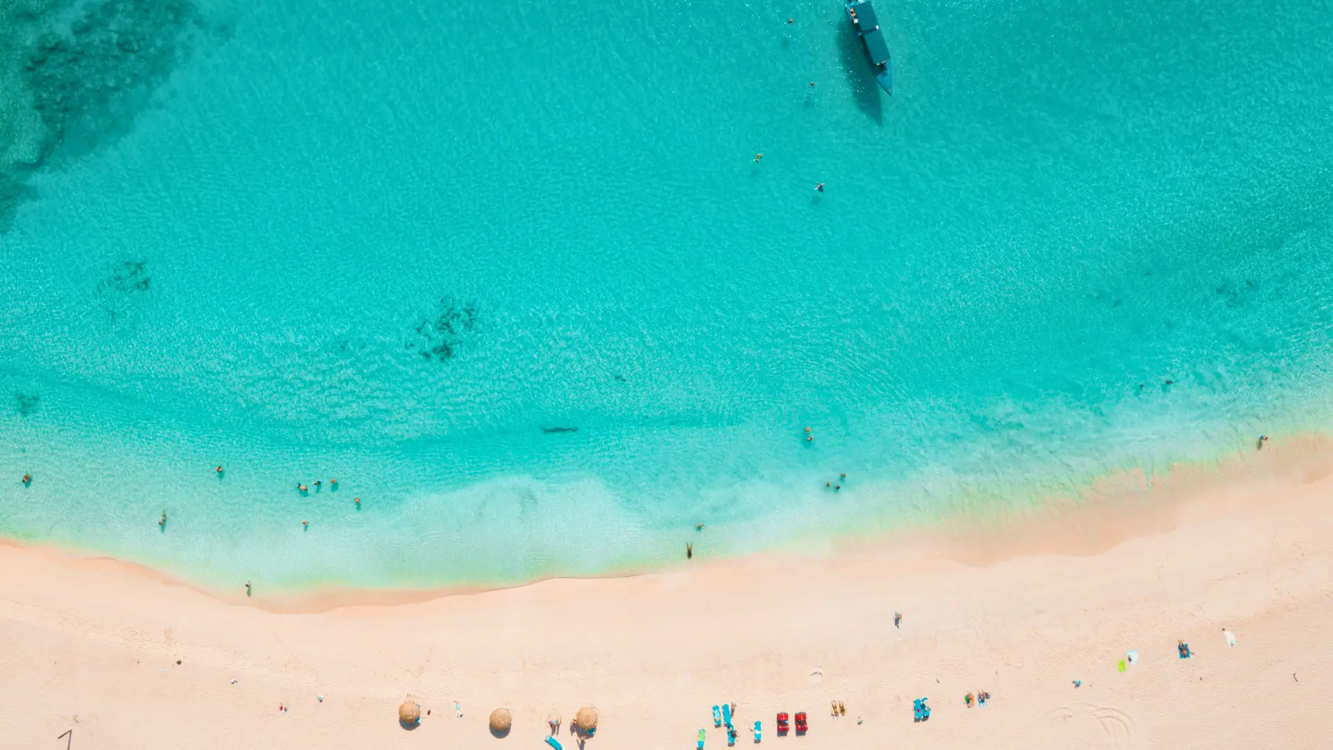 Aerial view of turquoise water and sandy beach in St Maarten with swimmers and anchored boat