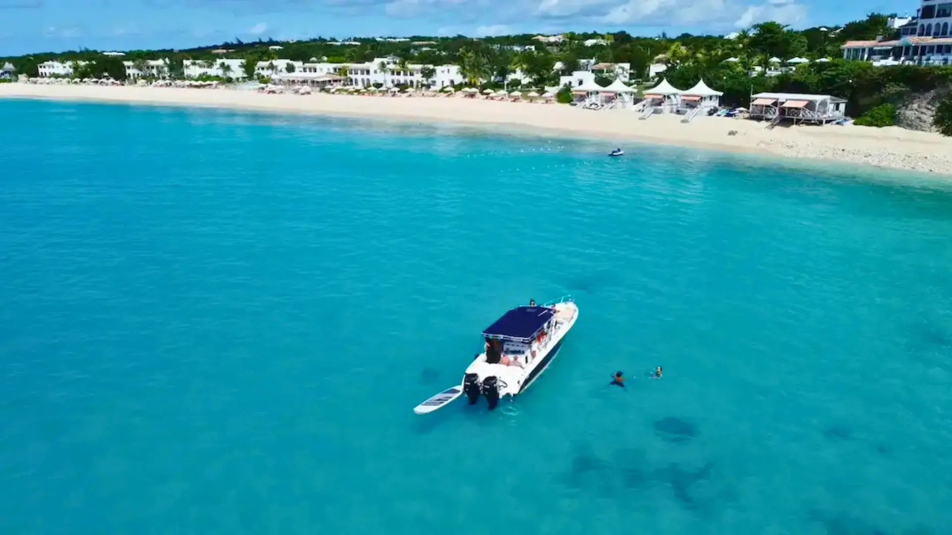 Private boat charter in Anguilla with guests swimming in clear turquoise water near beach