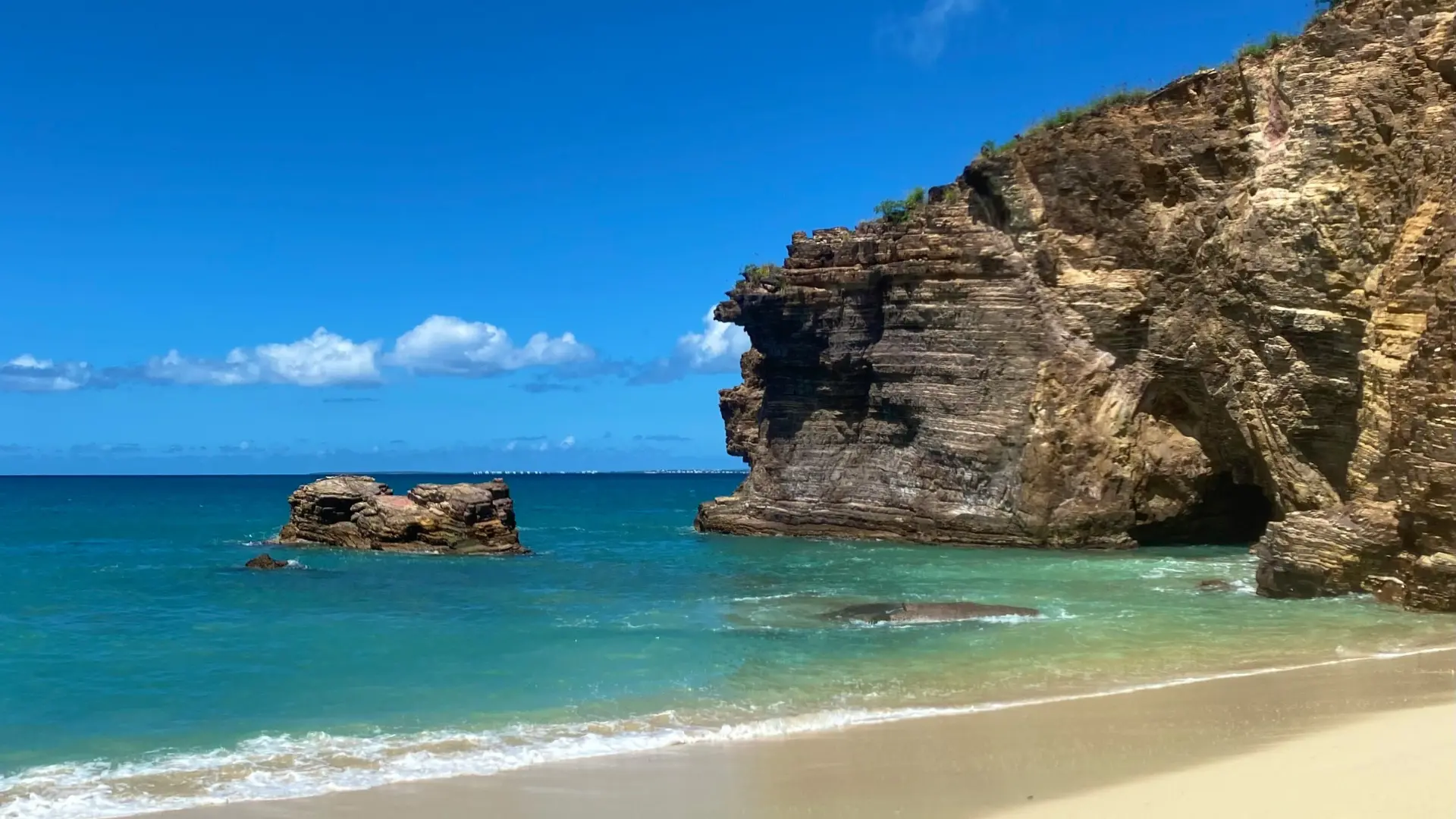 Baie Rouge beach in St Martin with cliffs, turquoise water, and quiet sandy shoreline