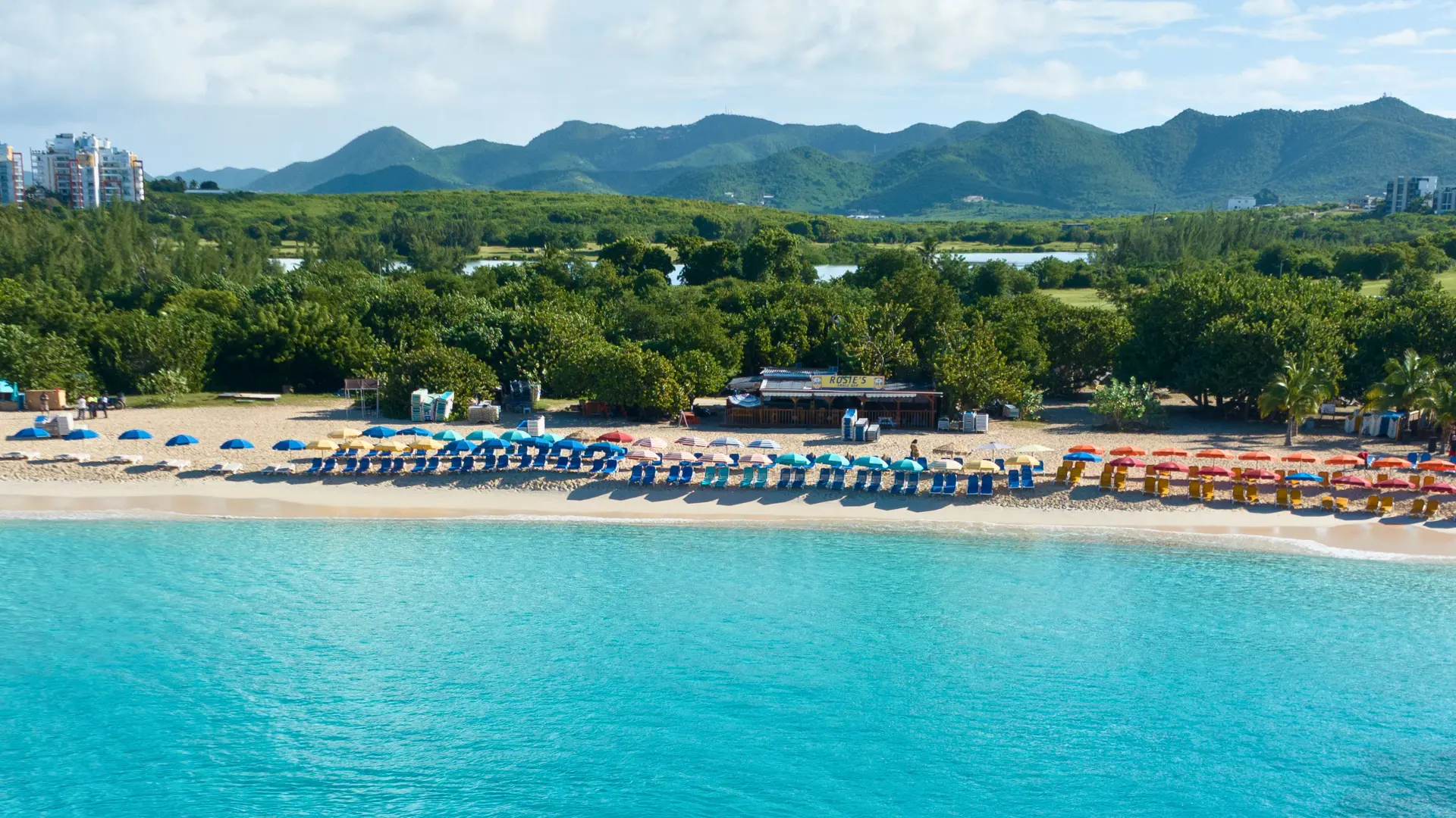 Beach with colorful umbrellas and calm turquoise water in St Maarten viewed from the sea
