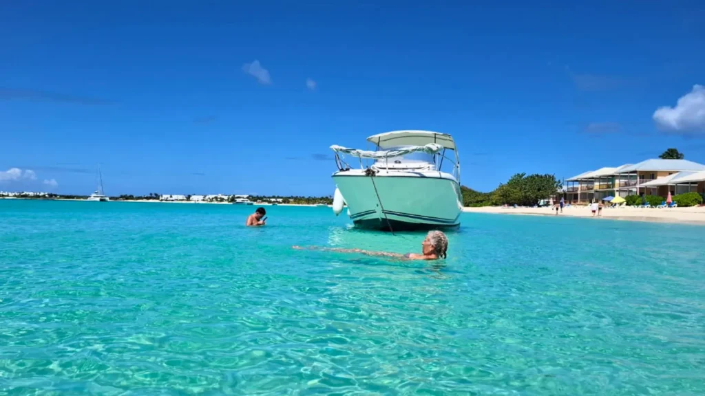 An elderly lady relaxes in shallow water in Anguilla whilst her grandson snorkels on a private boat charter.